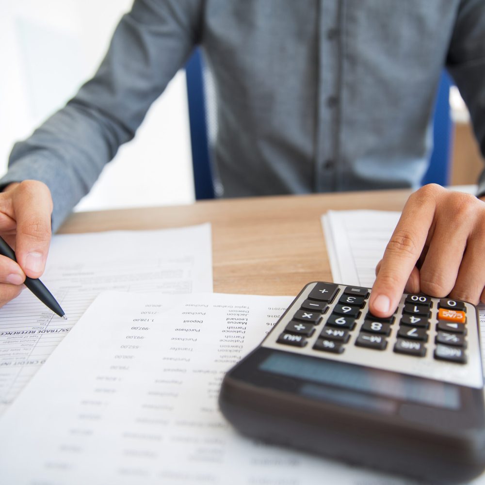 Close-up of male hands using calculator to examine report. Unrecognizable accountant counting profit. Businessman analyzing documents. Paperwork concept